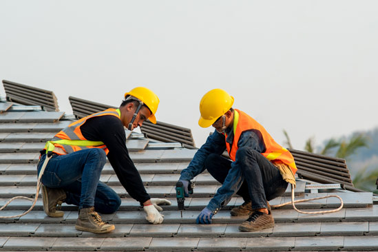 Construction worker wearing safety harness belt during working on roof structure of building on construction site,Roofer using air or pneumatic nail gun and installing concrete roof tile on top roof.